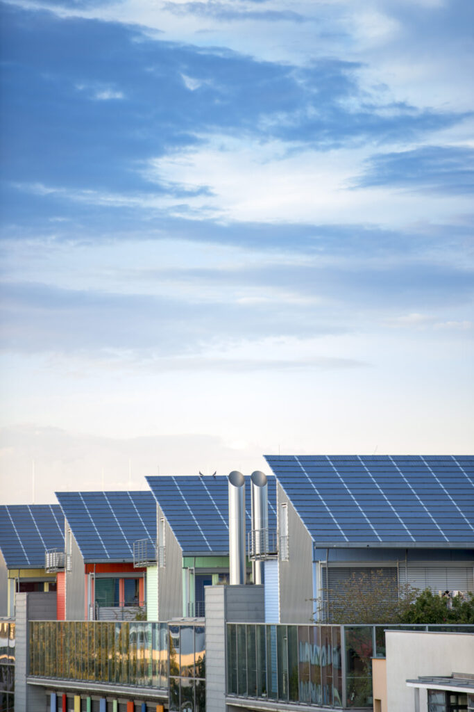 Row of modern solar panel homes using clean energy solutions under a bright blue sky.