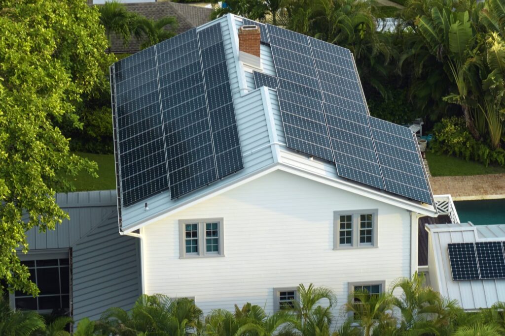 Modern white house with rooftop solar panels for home energy efficiency in a tropical setting.