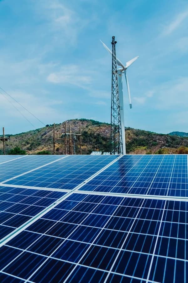 Hybrid renewable energy system with solar panels and wind turbine in a rural landscape.