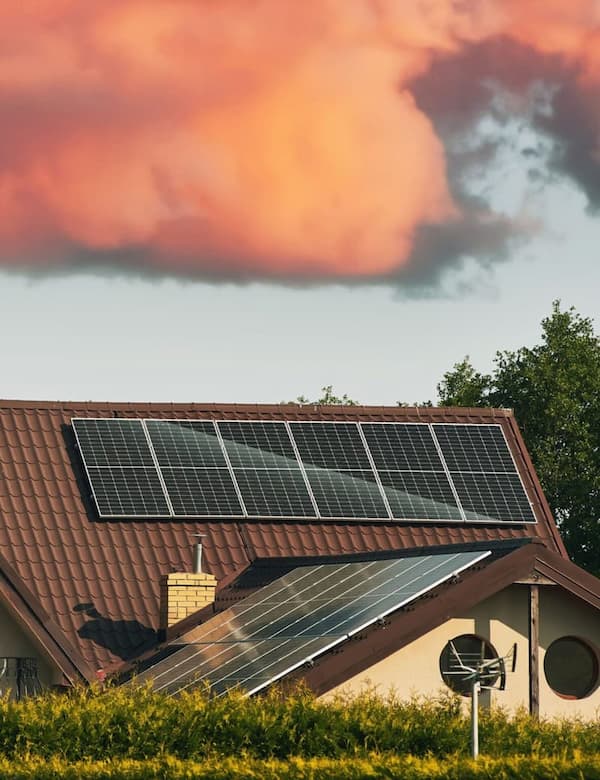 Modern private house with rooftop solar panels generating clean energy, showcasing renewable energy home solutions under a vibrant sunset sky.